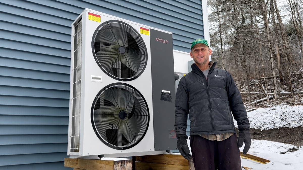 Installer standing beside an Apollo 6 ton air to water heat pump installed outdoors in winter.