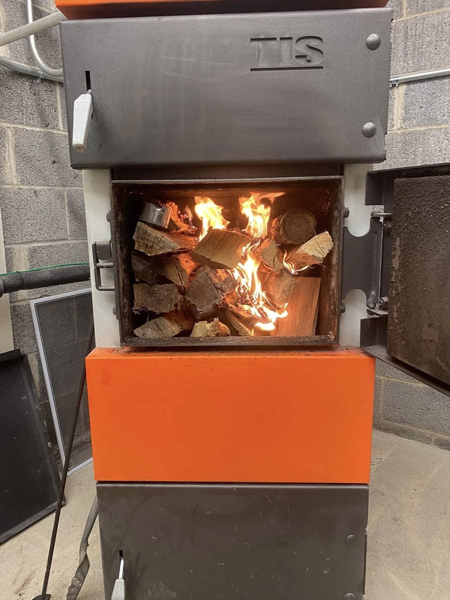 Close-up of a UNI wood boiler with its firebox open and split wood actively burning.