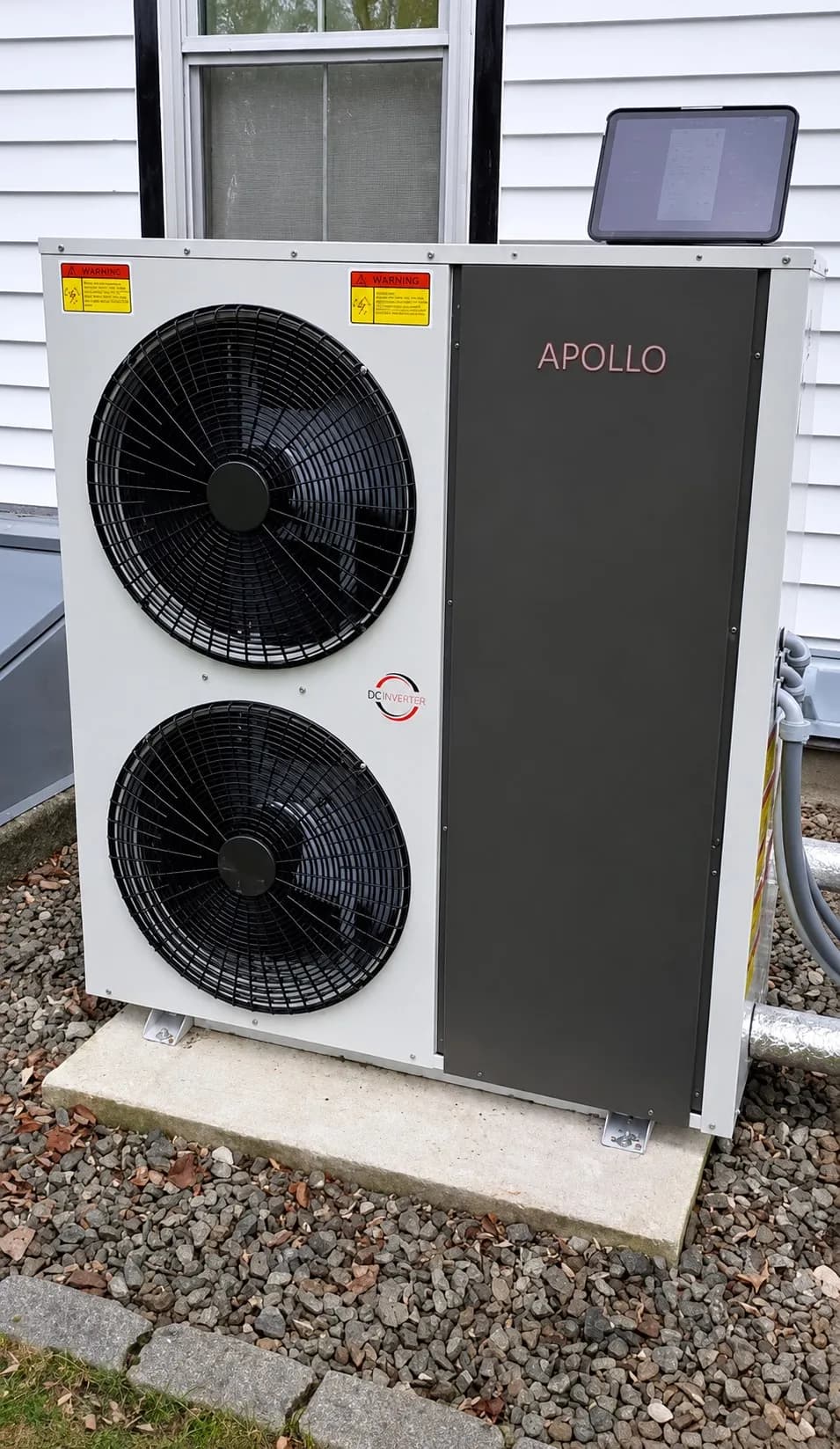 Apollo 5 ton air to water heat pump with a tablet positioned on the outdoor unit during commissioning.