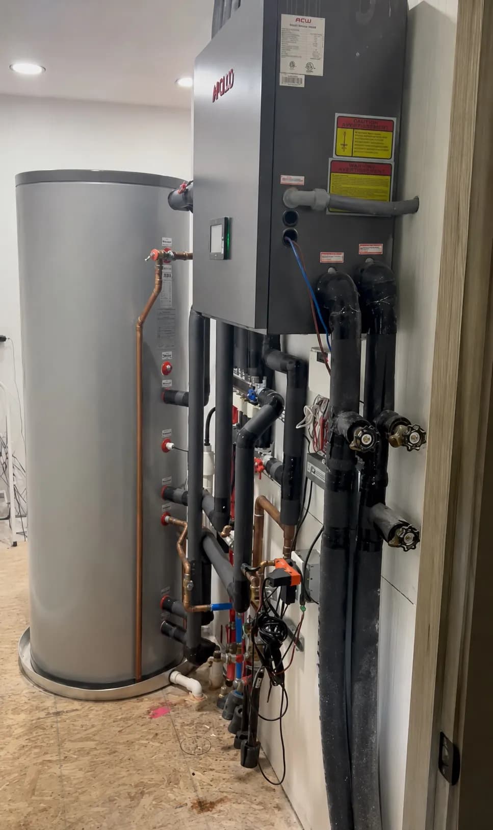 Apollo Hydro One hydronic station installed beside a vertical water storage tank with insulated piping.