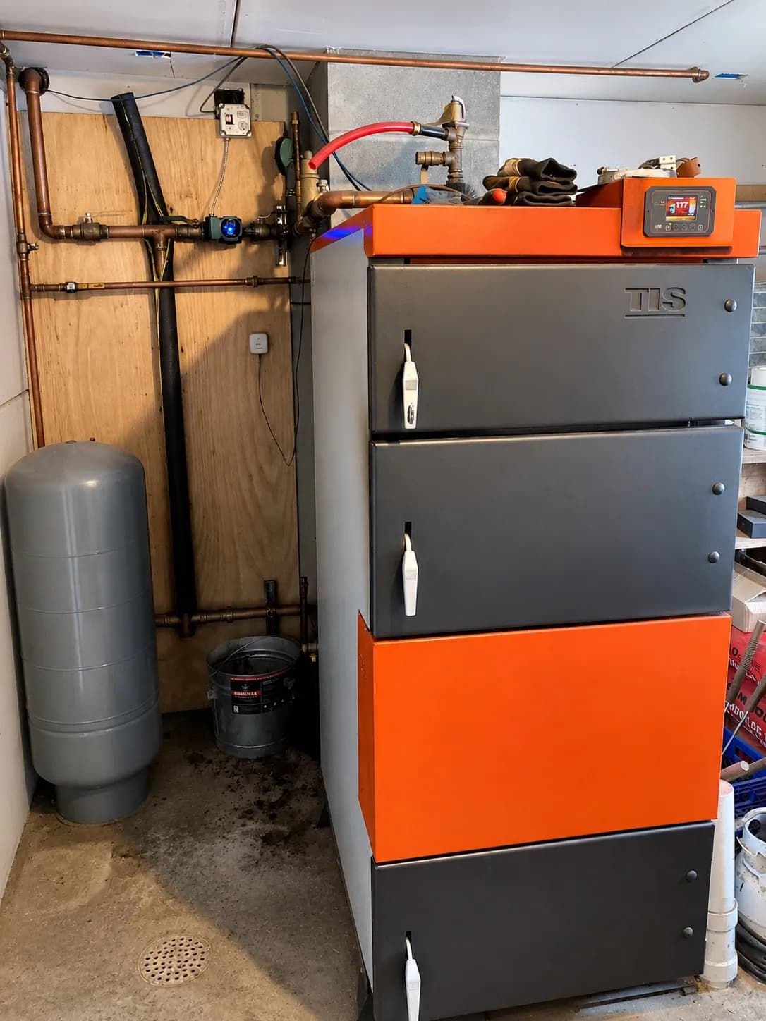 UNI wood boiler installed beside an expansion tank and copper hydronic piping in a mechanical room.