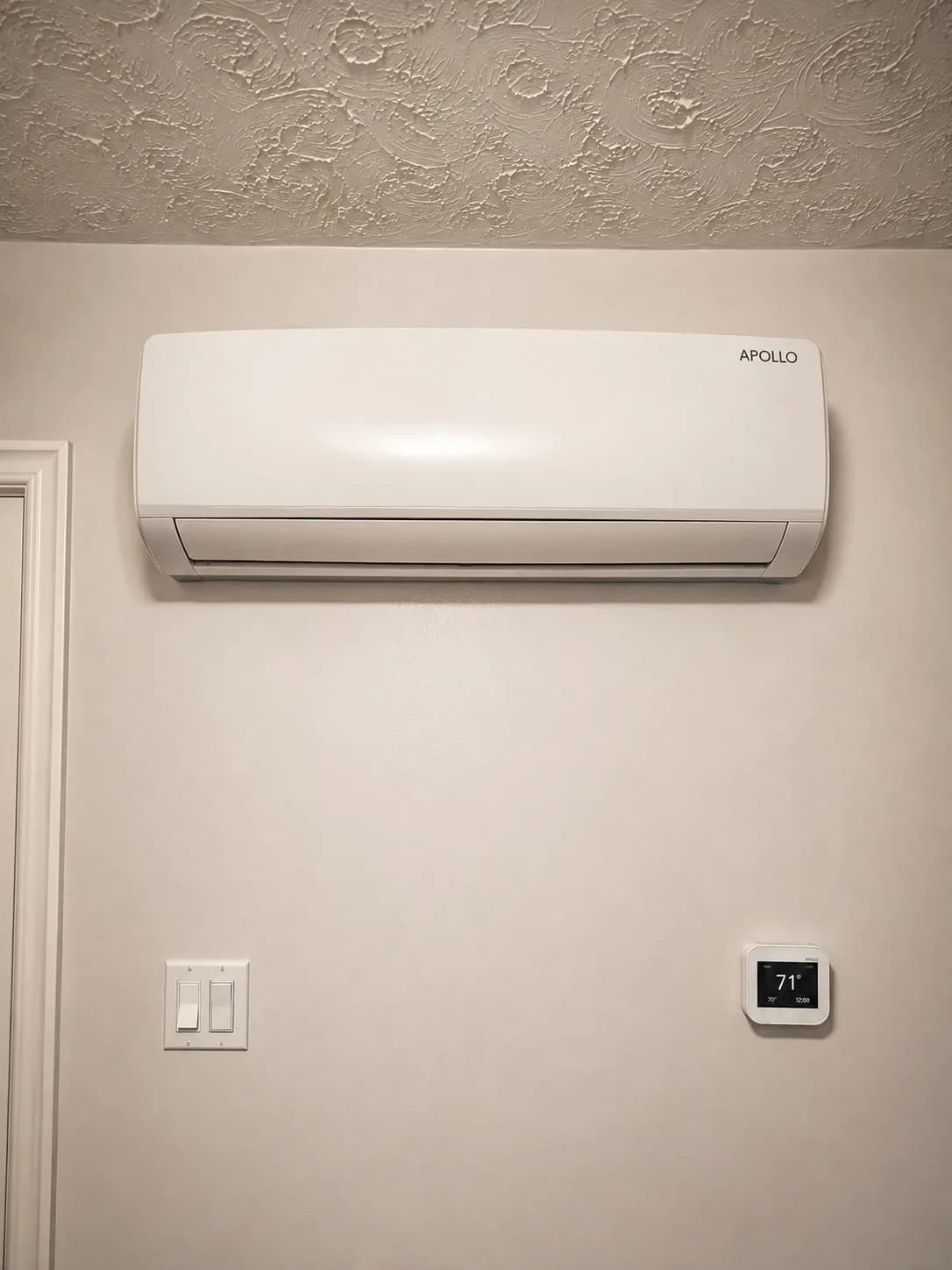 Apollo 1.5 ton wall fan coil installed above a wall-mounted thermostat.