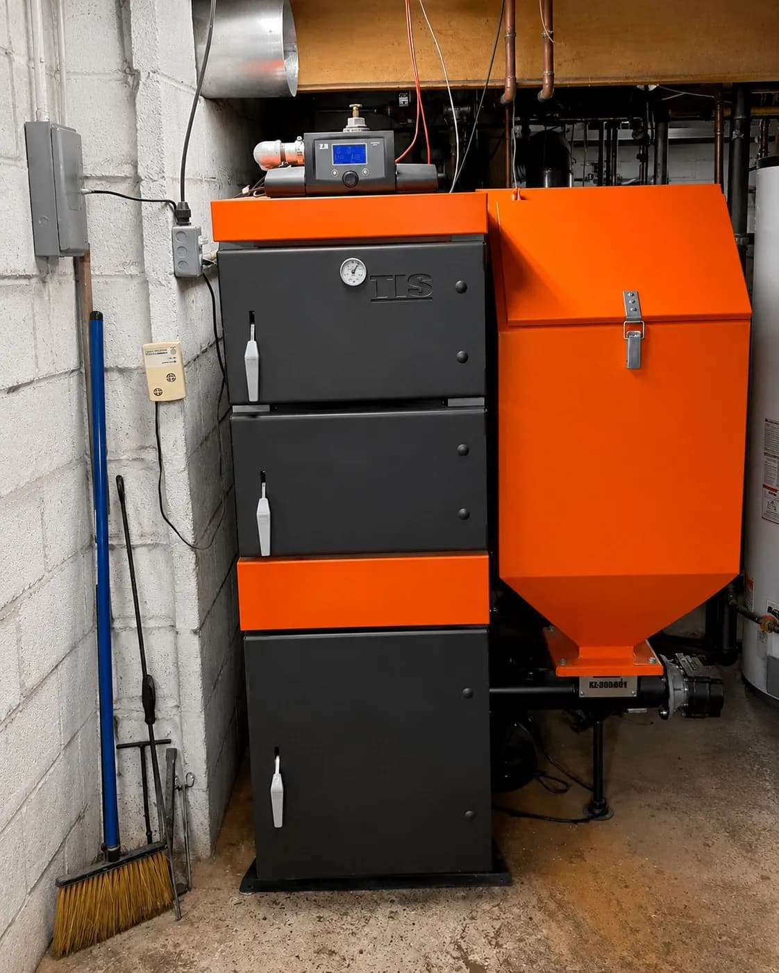 MBTEK boiler system with a black and orange cabinet unit and orange hopper in a utility basement.