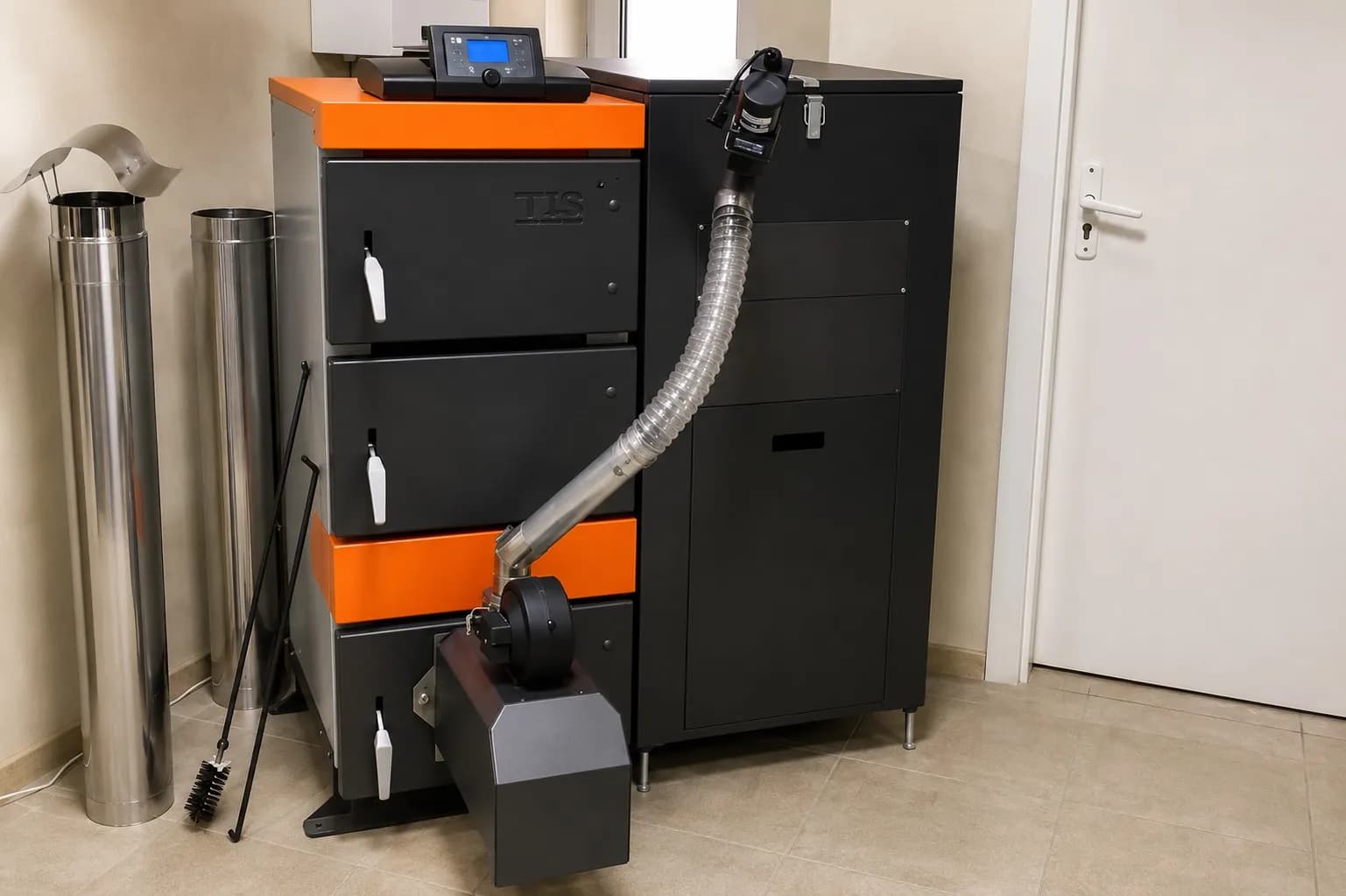Black and orange pellet boiler connected to a black fuel hopper and auger in a finished mechanical room.